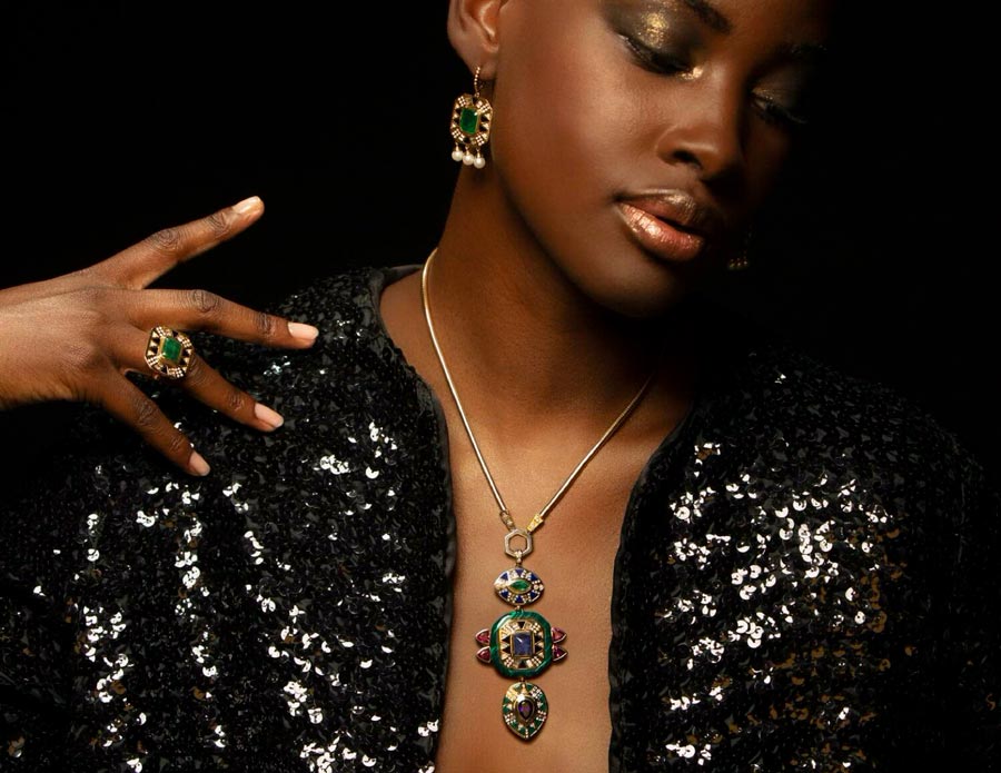 Woman in black sequin top looking down with right hand on shoulder wearing rings, earrings and pendant necklace for Cleopatra's Vault