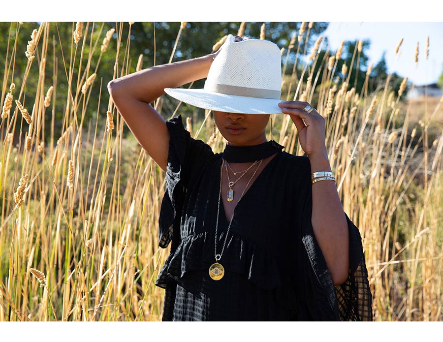 Woman in nature wearing white hat that covers her eyes wearing pendant necklaces, earrings, bracelets, rings for Good Juju Collection